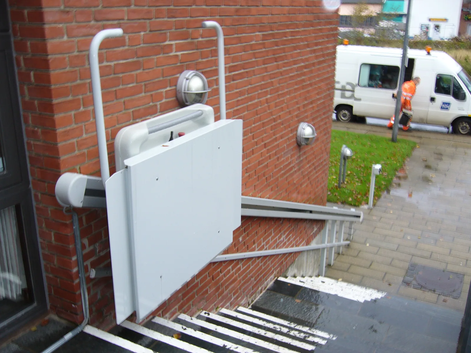 Plateaulift rechte trap opgevouwen tegen muur in parkeerstand — 350 mm uitsteek, servicevoertuig zichtbaar