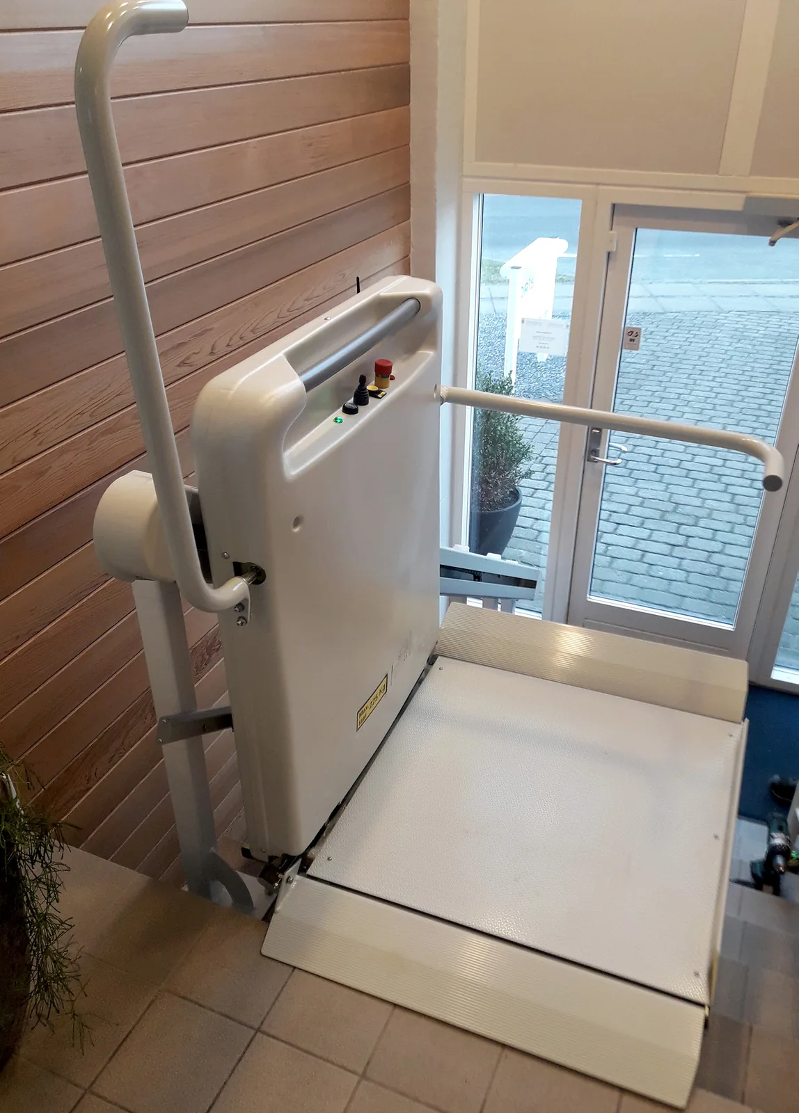 Rolstoel-traplift met BCRL Raise & Lower mechaniek — platform daalt verticaal aan de onderzijde van de trap